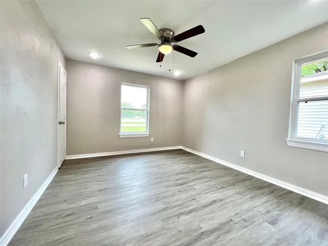 an empty room with wooden floor fan and windows
