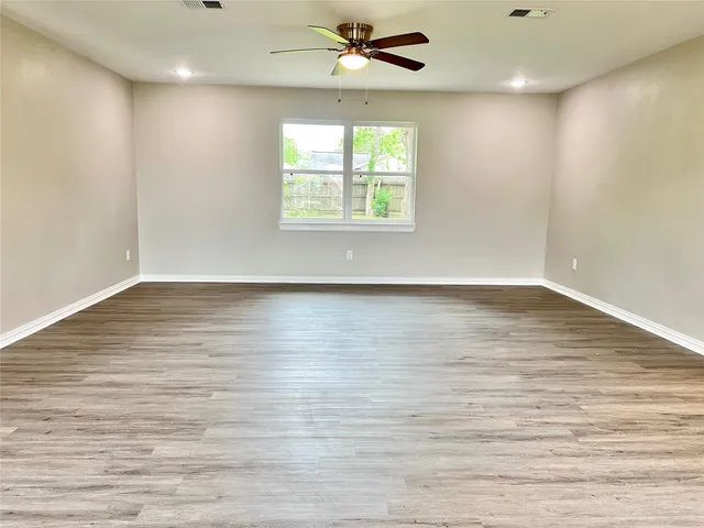 an empty room with wooden floor a ceiling fan and windows