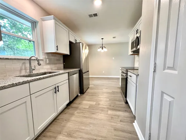 a kitchen with stainless steel appliances granite countertop a refrigerator a sink dishwasher a stove and white countertops with wooden floor