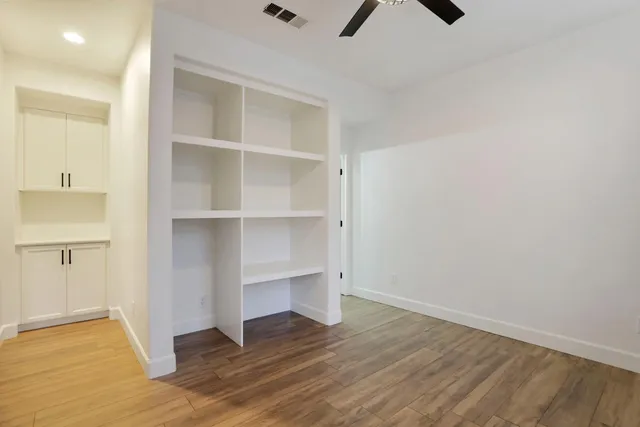 an empty room with wooden floor fan and windows
