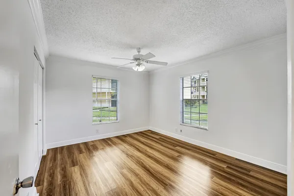 a view of an empty room with wooden floor and a ceiling fan