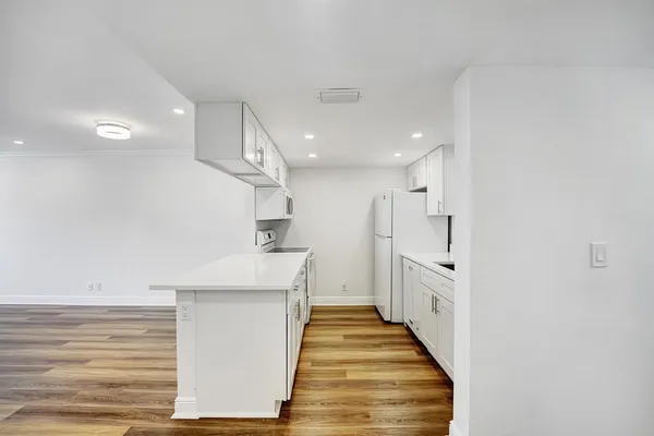 a large white kitchen with a refrigerator a sink dishwasher a stove and white cabinets with wooden floor