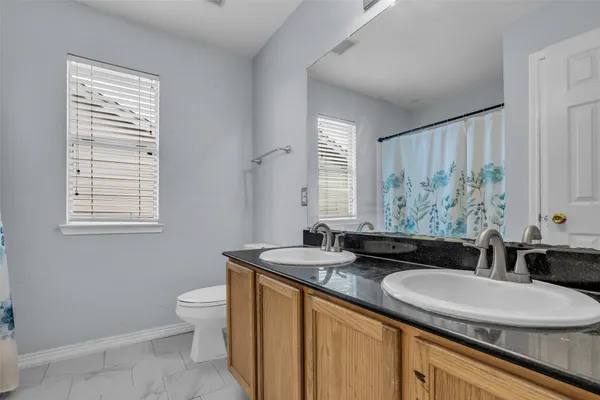 a bathroom with a granite countertop sink a toilet a mirror and window