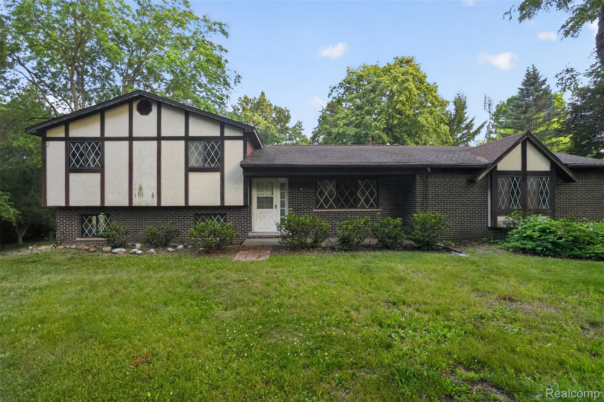 Brick and Tudor-style exterior featuring diamond-pane windows, a prominent front entry, and mature landscaping