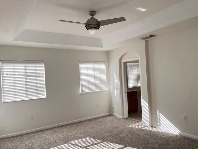 an empty room with chandelier fan and windows