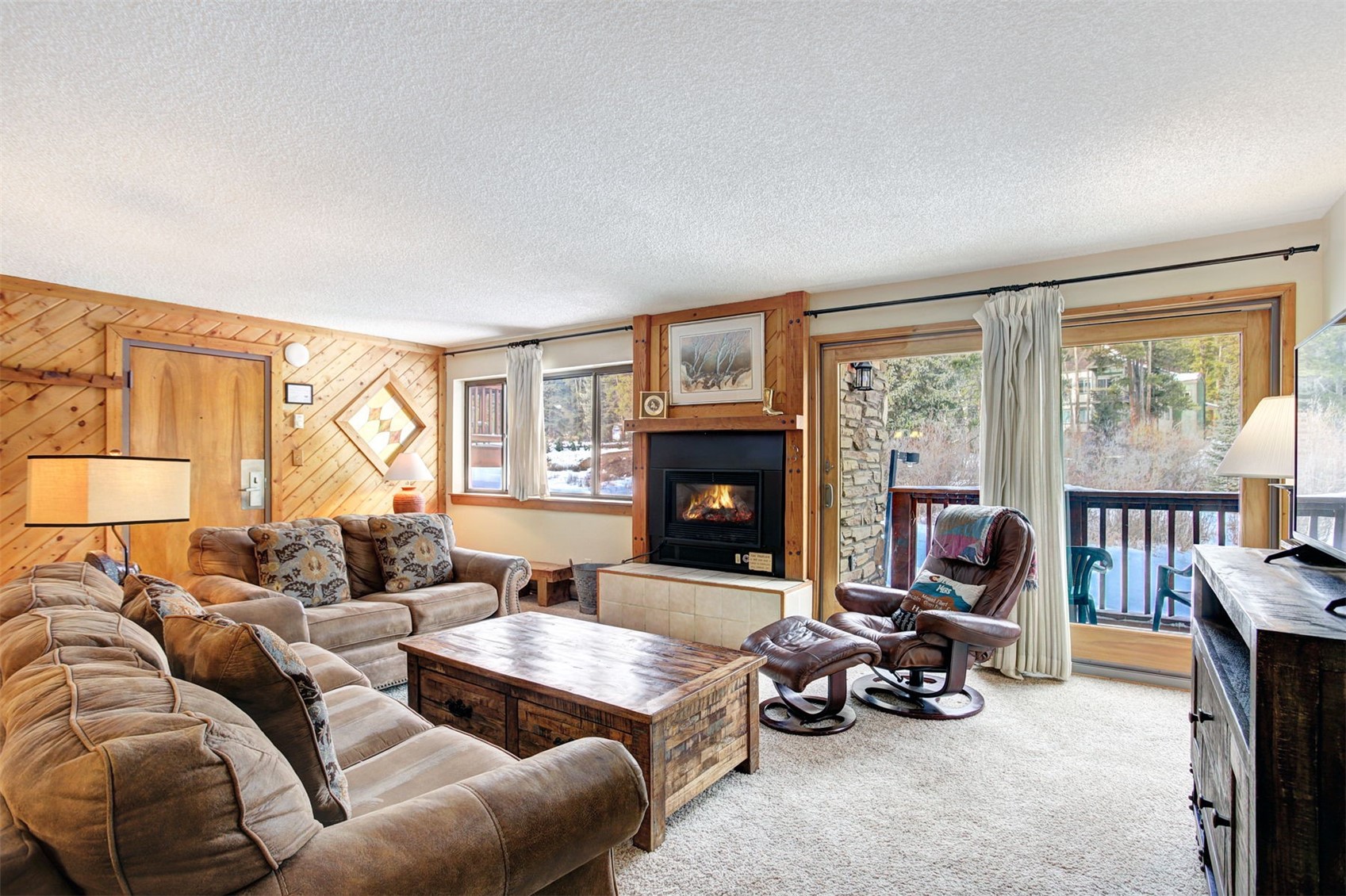 400 4 O Clock Road, Unit A Breckenridge, CO 80424 - Photo 4 of 31 Living room with a textured ceiling, wood walls, light colored carpet, and a tiled fireplace