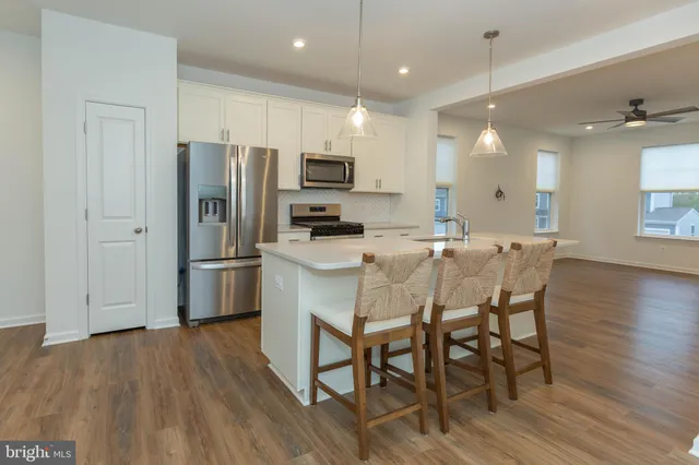 a kitchen with stainless steel appliances a refrigerator a stove a sink a dining table and chairs with wooden floor