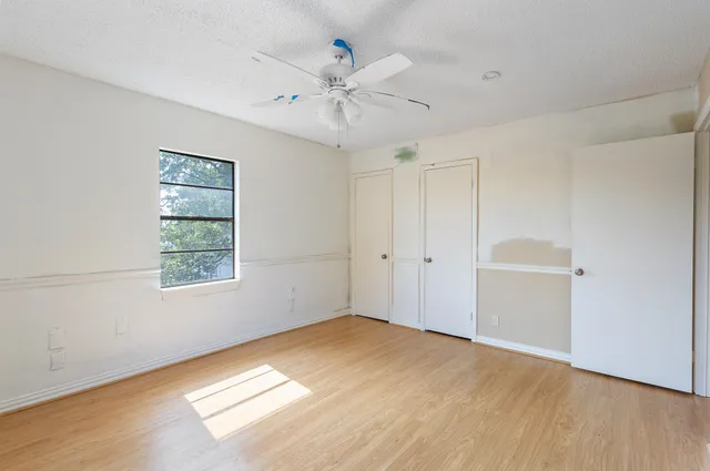 an empty room with wooden floor ceiling fan and windows