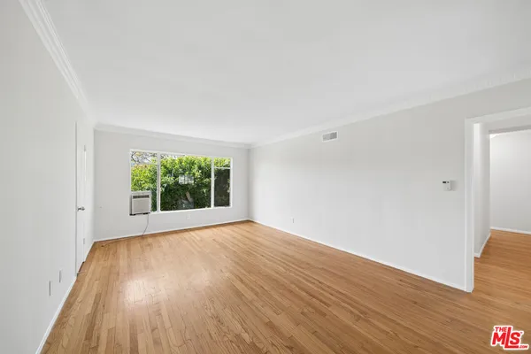 a view of an empty room with wooden floor and a window