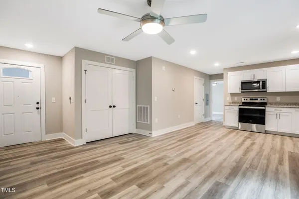 an empty room with wooden floor a ceiling fan a kitchen view and a fireplace
