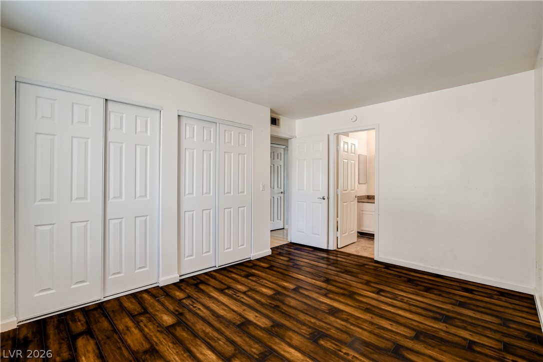 7200 West Pirates Cove Road, Unit 1050 Las Vegas, NV 89145 - Photo 14 of 24 Unfurnished bedroom with two closets, dark wood-style floors, and ensuite bathroom