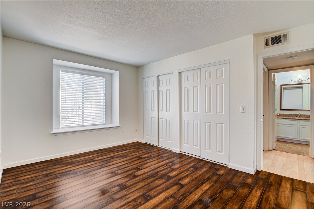 7200 West Pirates Cove Road, Unit 1050 Las Vegas, NV 89145 - Photo 15 of 24 Unfurnished bedroom with two closets, dark wood-style floors, and a textured ceiling