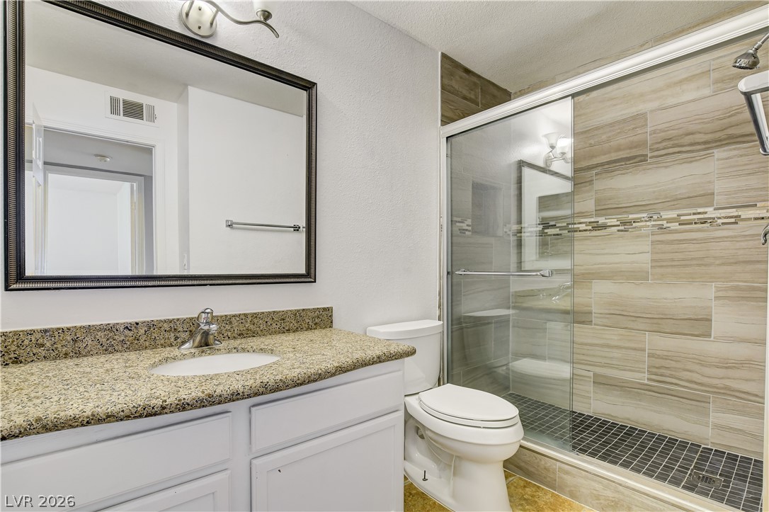 7200 West Pirates Cove Road, Unit 1050 Las Vegas, NV 89145 - Photo 18 of 24 Full bathroom featuring vanity, a textured wall, a shower stall, and a textured ceiling