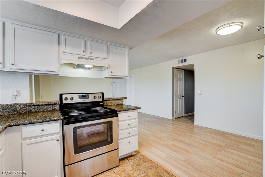 7200 West Pirates Cove Road, Unit 1050 Las Vegas, NV 89145 - Photo 6 of 24 Kitchen with stainless steel range with electric stovetop, white cabinets, dark stone countertops, and light wood-style floors