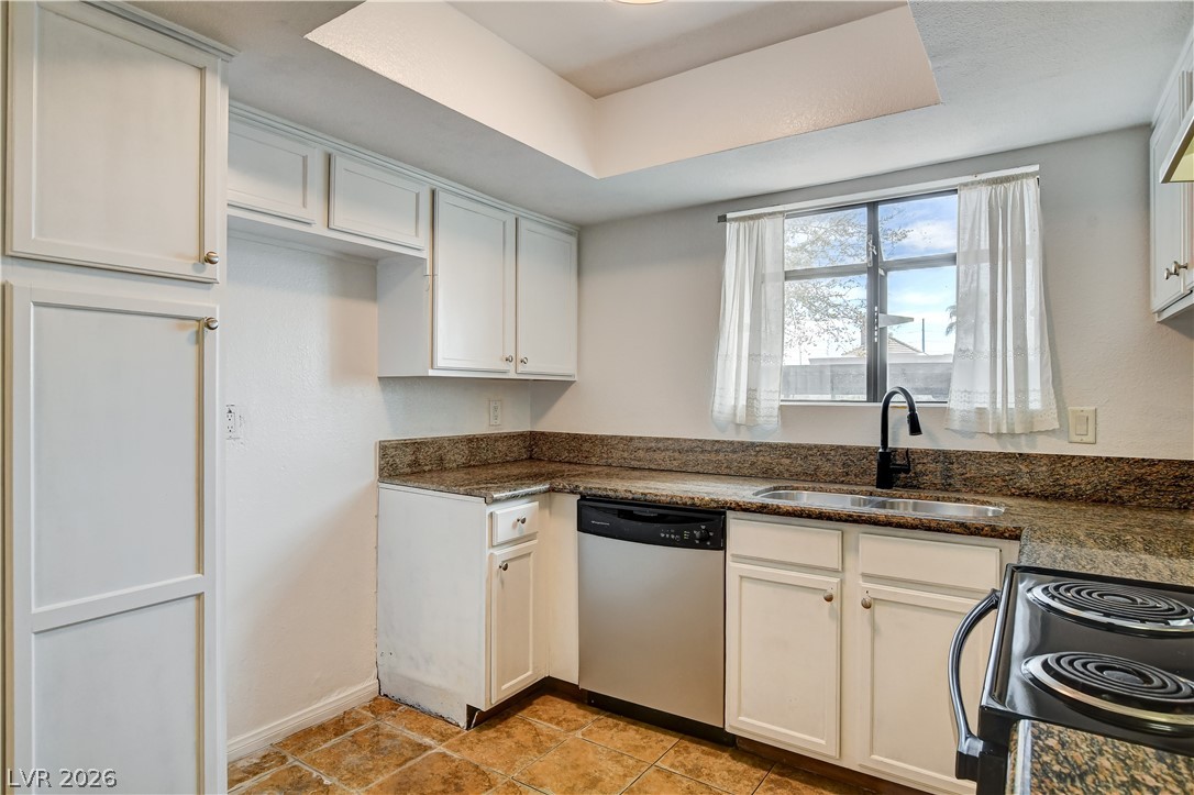 7200 West Pirates Cove Road, Unit 1050 Las Vegas, NV 89145 - Photo 7 of 24 Kitchen featuring stainless steel dishwasher, black electric range oven, white cabinetry, a tray ceiling, and light tile patterned floors