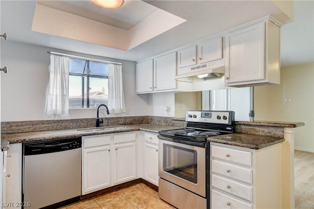 7200 West Pirates Cove Road, Unit 1050 Las Vegas, NV 89145 - Photo 8 of 24 Kitchen featuring stainless steel appliances, white cabinets, dark stone countertops, a peninsula, and a raised ceiling
