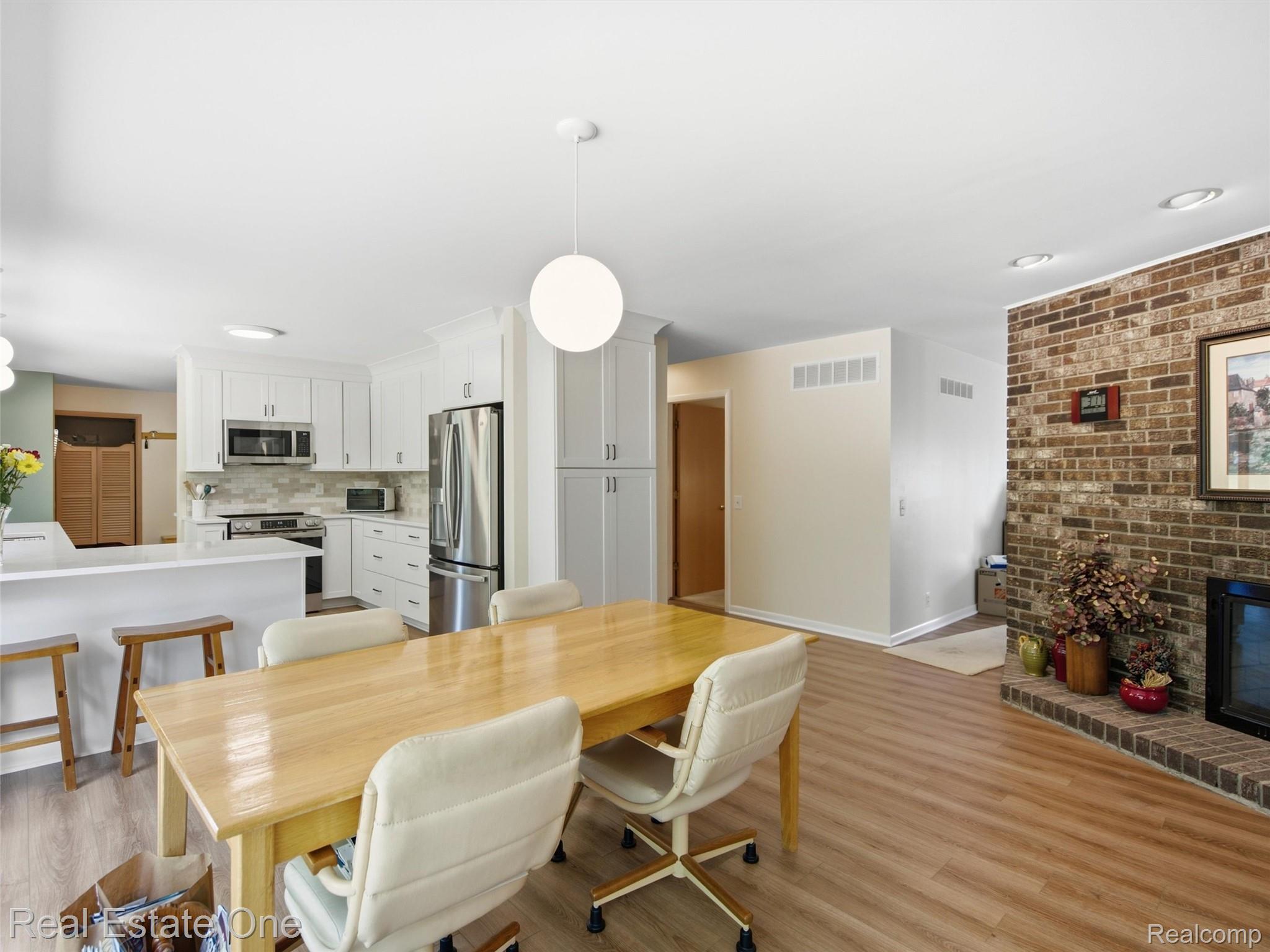 2626 West Wattles Road Troy, MI 48098 - Photo 12 of 65 White shaker cabinetry, stainless steel appliances, brick fireplace surround, wood-finish flooring, and a breakfast bar