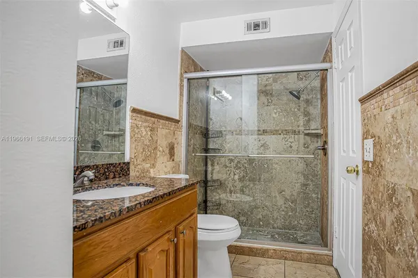 a bathroom with a granite countertop sink a toilet a mirror and shower