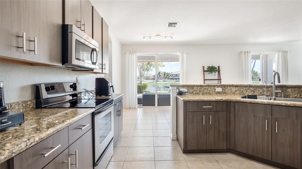 19470 Stonebrook Street Weston, FL 33332 - Photo 11 of 44 a large kitchen with stainless steel appliances granite countertop a sink and dishwasher a stove with wooden cabinets