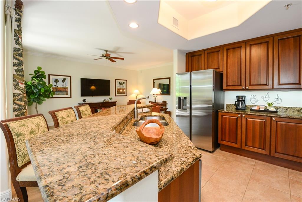 975 Sandpiper Street, Unit A104 Naples, FL 34102 - Photo 11 of 33 a kitchen with granite countertop a refrigerator a stove a sink dishwasher and wooden cabinets with wooden floor