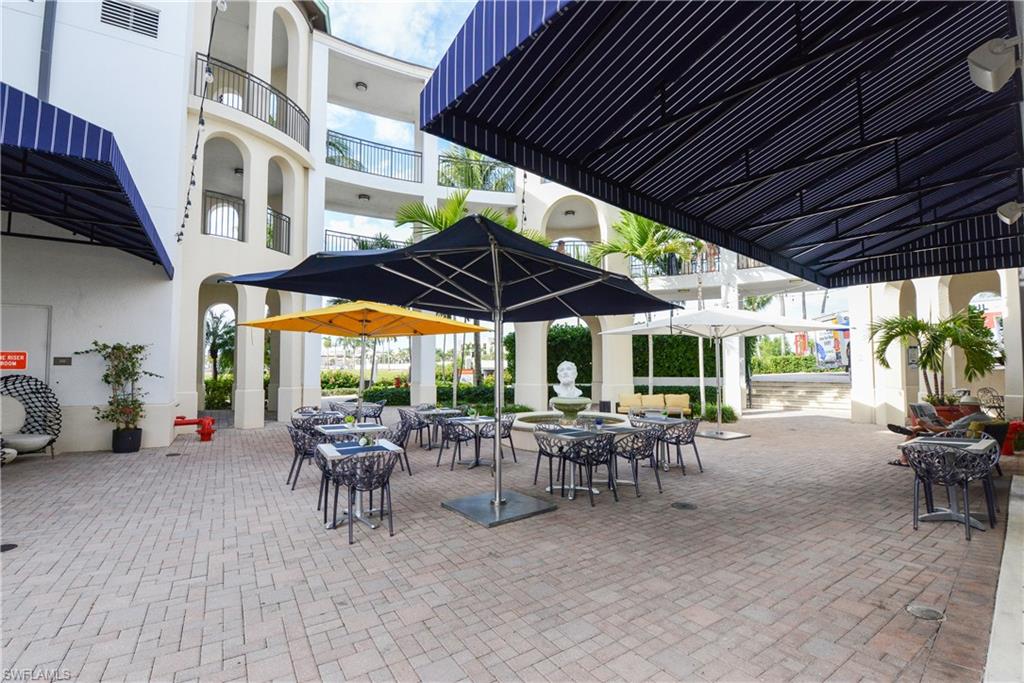 975 Sandpiper Street, Unit A104 Naples, FL 34102 - Photo 32 of 33 a view of a patio with table and chairs under an umbrella with a table and chairs under an umbrella