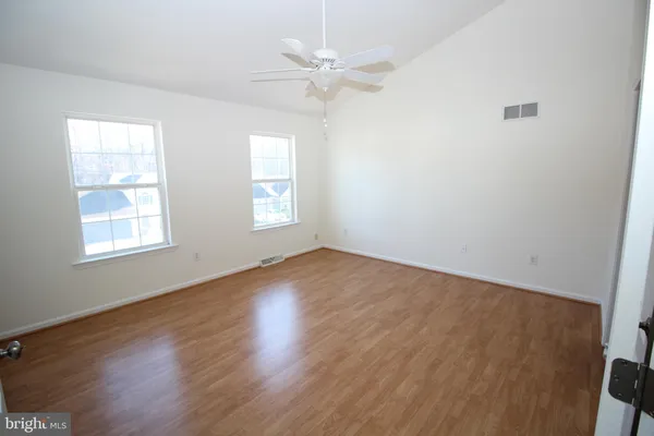 an empty room with wooden floor fan and windows