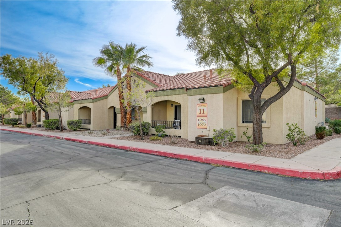 7885 West Flamingo Road, Unit 1071 Las Vegas, NV 89147 - Photo 2 of 28 A well-maintained street leads to an attractive apartment complex with a tiled roof.