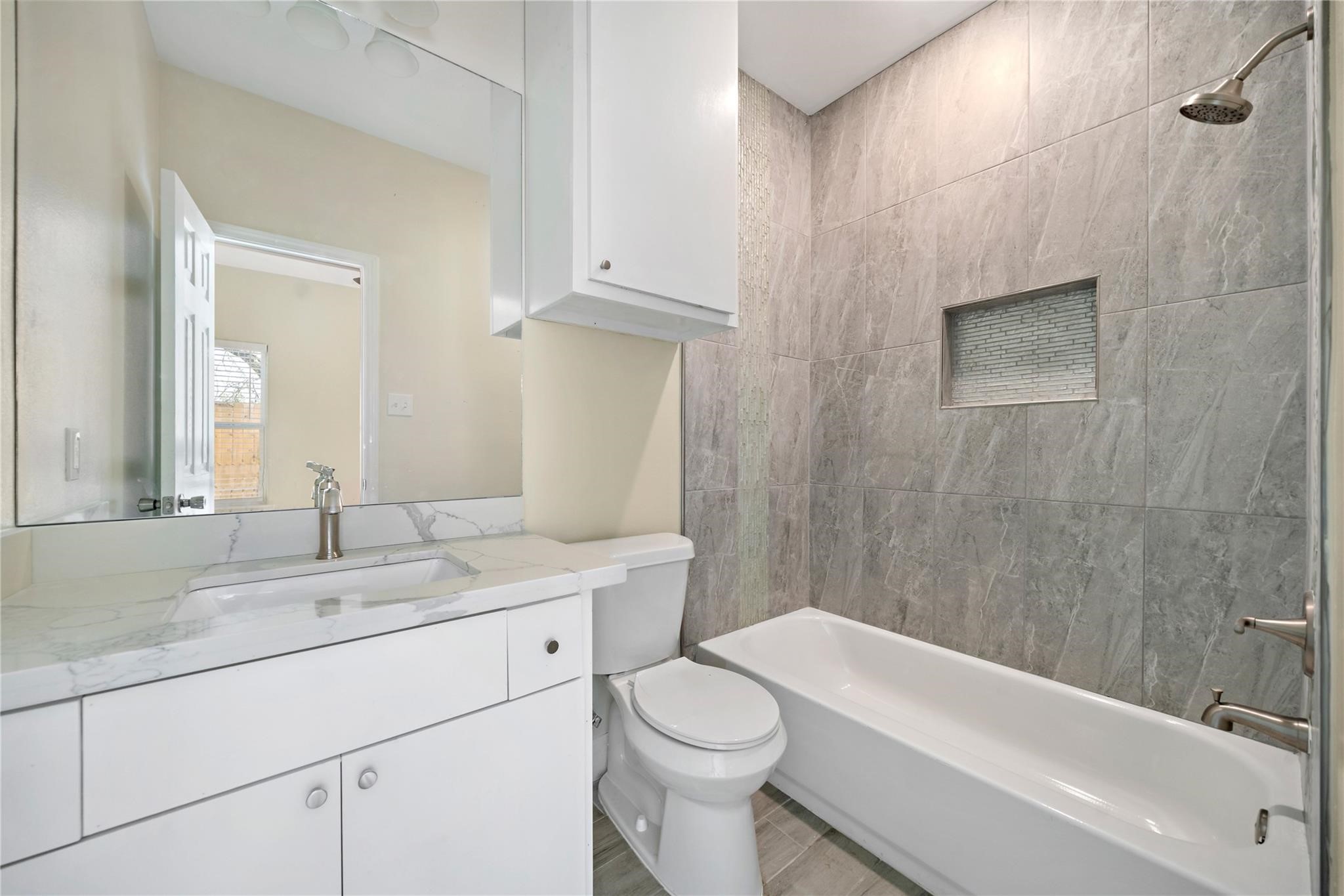 5618 Ridgeway Drive, Unit B Houston, TX 77033 - Photo 7 of 9 This bathroom features modern gray tile with a built-in shower niche, a sleek white vanity with a marble countertop, and ample cabinet storage. The bright, clean design offers a contemporary feel.