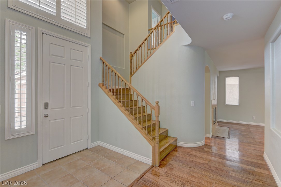 1813 Snow Spring Lane Las Vegas, NV 89134 - Photo 4 of 37 A welcoming entry features a grand staircase and light-filled windows, showcasing polished wood flooring throughout.