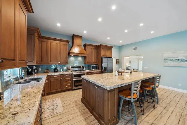 a large kitchen with stainless steel appliances granite countertop a stove a sink dishwasher and a refrigerator with wooden floor