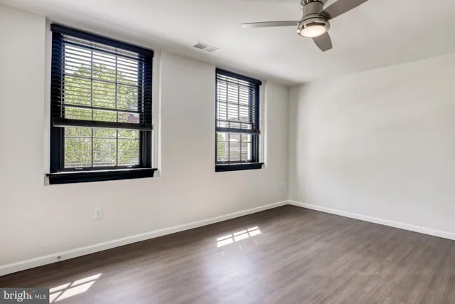 an empty room with wooden floor fan and windows