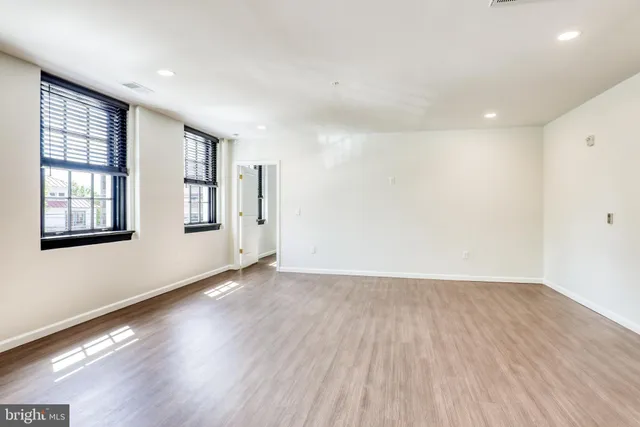 a view of an empty room with wooden floor and windows