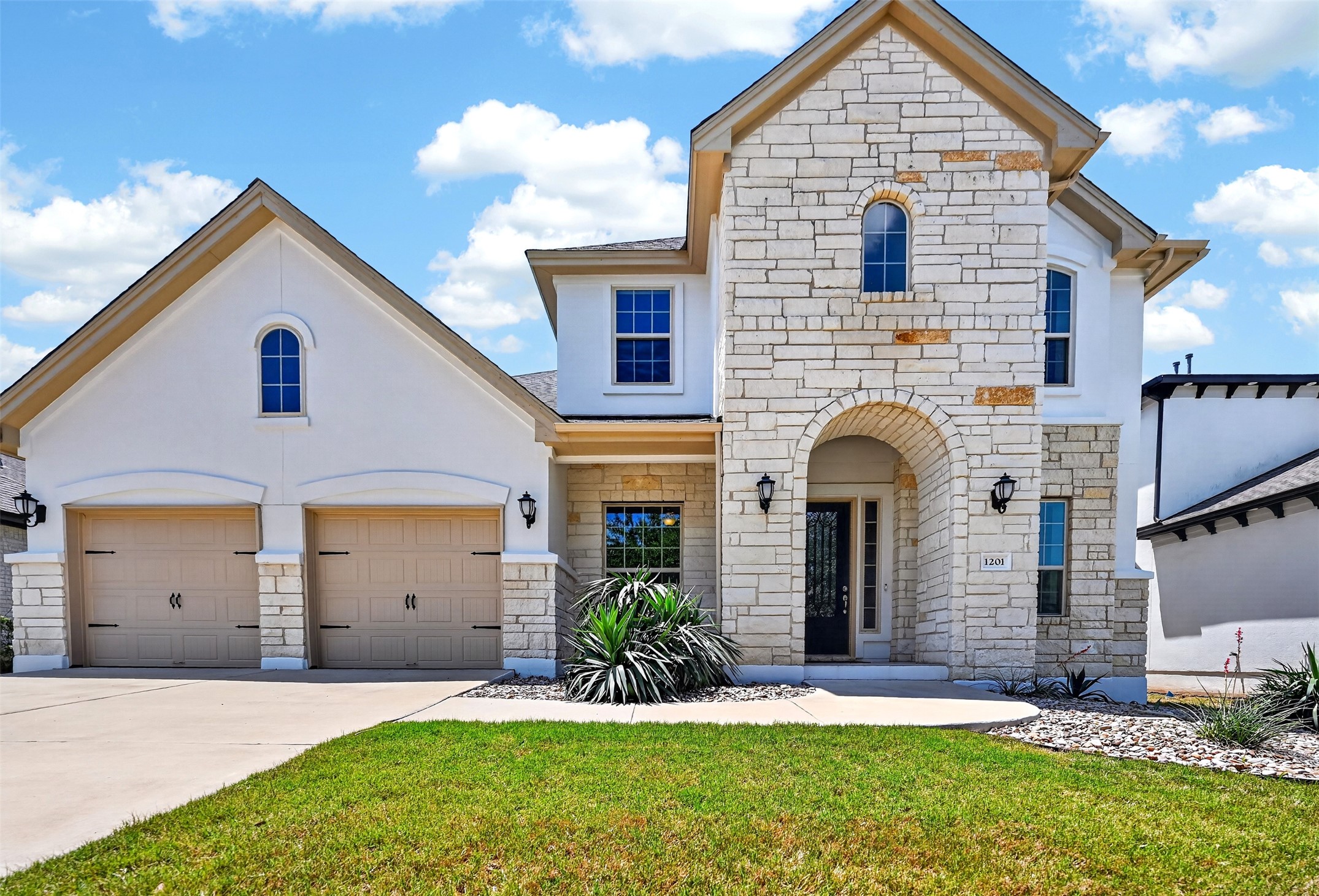 1201 Positano Pass Leander, TX 78641 - Photo 1 of 40 Stucco and stone exterior featuring an arched entryway, decorative coach lights, and a two-car garage with arched window above