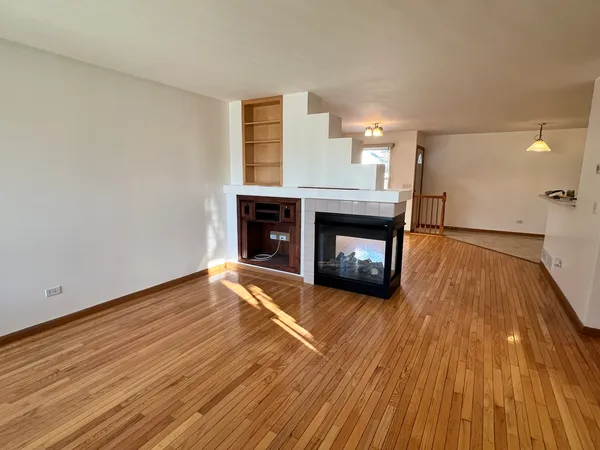 a view of an empty room with wooden floor fireplace and a window