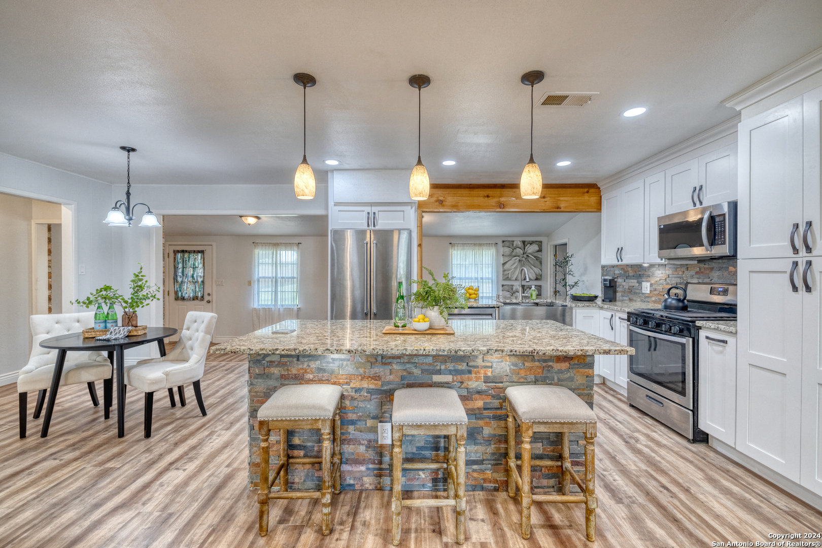 a kitchen with stainless steel appliances granite countertop a stove a refrigerator a kitchen island a dining table and chairs with wooden floor