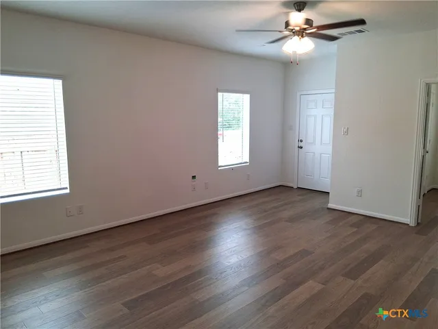 an empty room with wooden floor fan and windows
