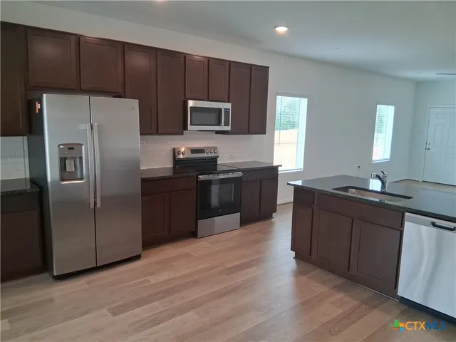 a kitchen with stainless steel appliances wooden cabinets a refrigerator a sink a stove a microwave and wooden floors
