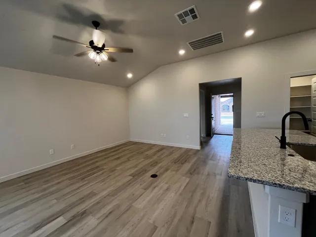 an empty room with wooden floor and kitchen view