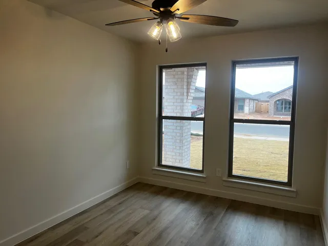 an empty room with wooden floor fan and windows