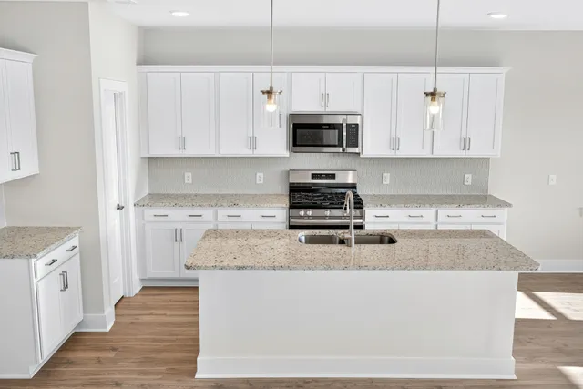 a kitchen with stainless steel appliances granite countertop a sink a stove a refrigerator and white cabinets