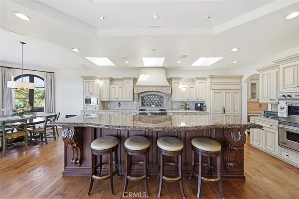 a kitchen with stainless steel appliances kitchen island granite countertop a dining table chairs and wooden floor