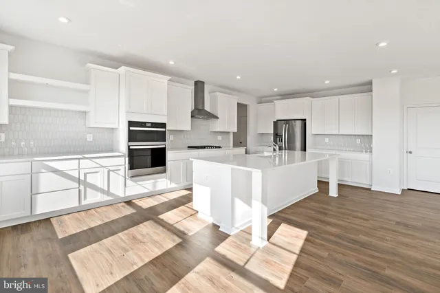 a kitchen with stainless steel appliances granite countertop a stove a sink dishwasher a refrigerator and white cabinets with wooden floor