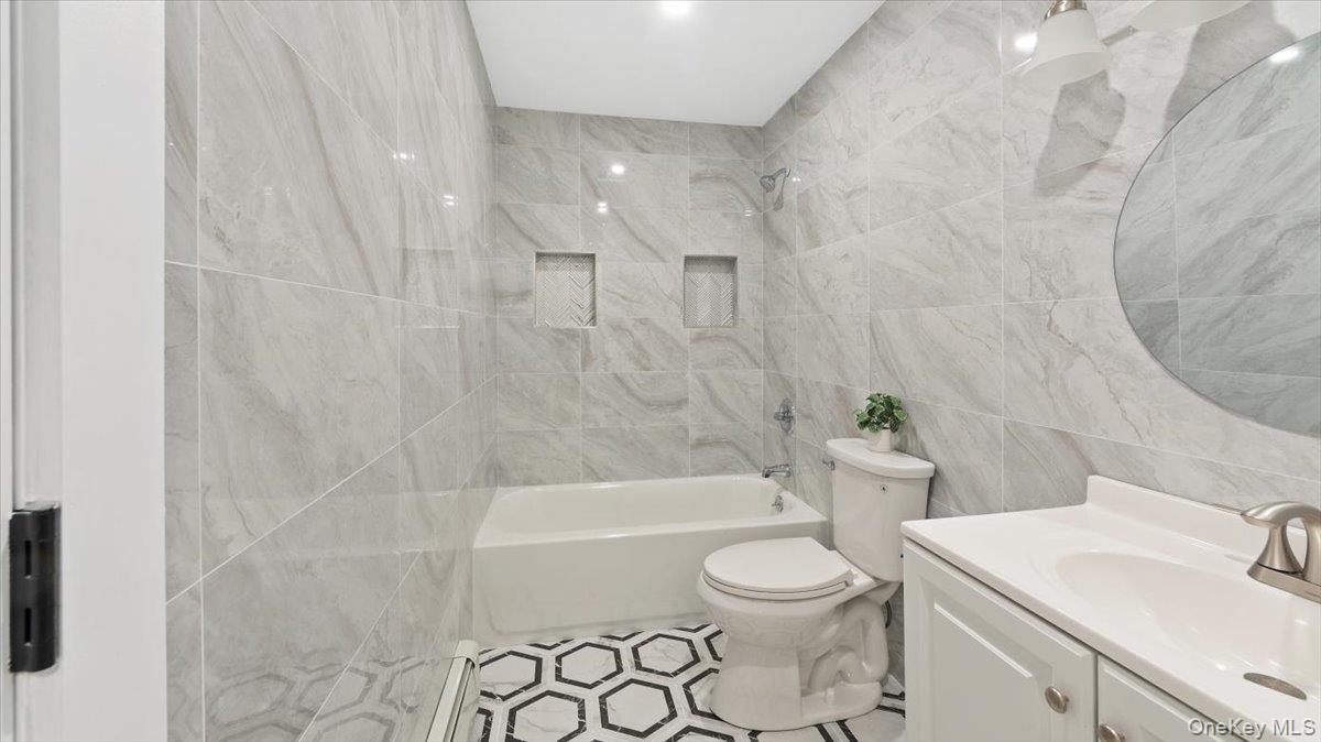 77 Friendly Road Mahopac, NY 10541 - Photo 17 of 36 Main Floor Bathroom featuring tile walls, vanity, shower / bathtub combination, a baseboard heating unit, and tile patterned floors