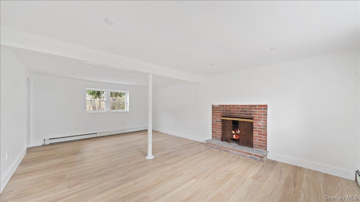 77 Friendly Road Mahopac, NY 10541 - Photo 26 of 36 Unfurnished Family Room or Bedroom with a brick fireplace, light wood-type flooring, and a baseboard heating unit