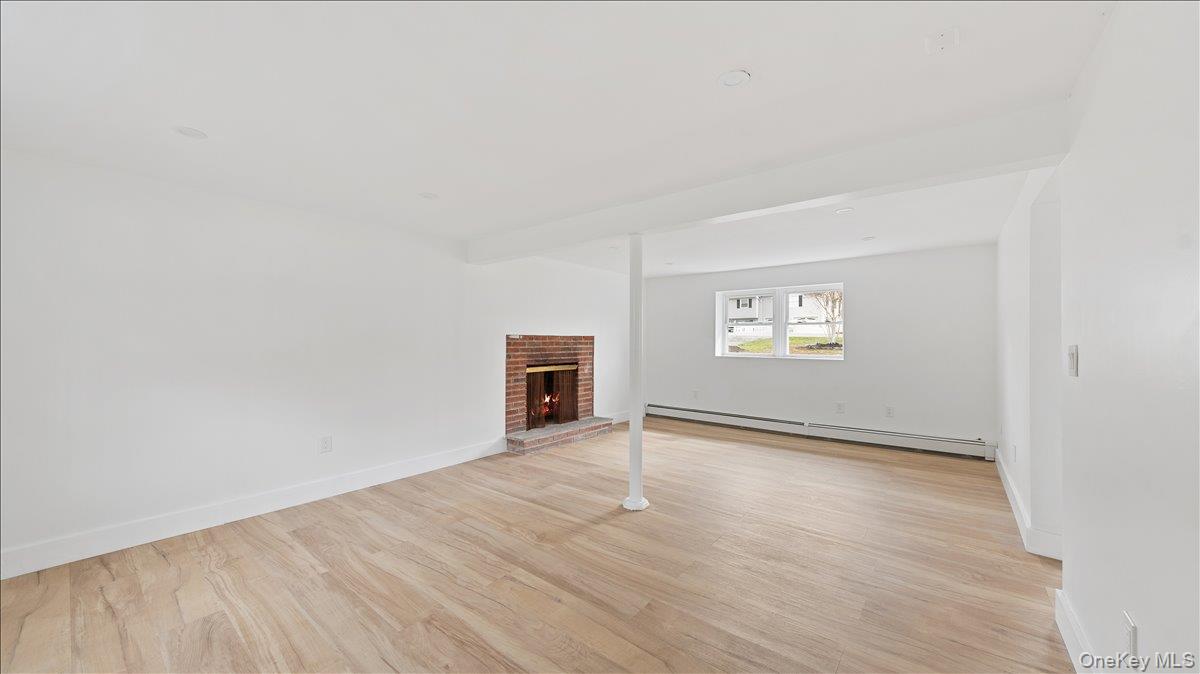 77 Friendly Road Mahopac, NY 10541 - Photo 29 of 36 Unfurnished Family Room or Bedroom with featuring light wood-style floors, a brick fireplace, a baseboard radiator, and beam ceiling