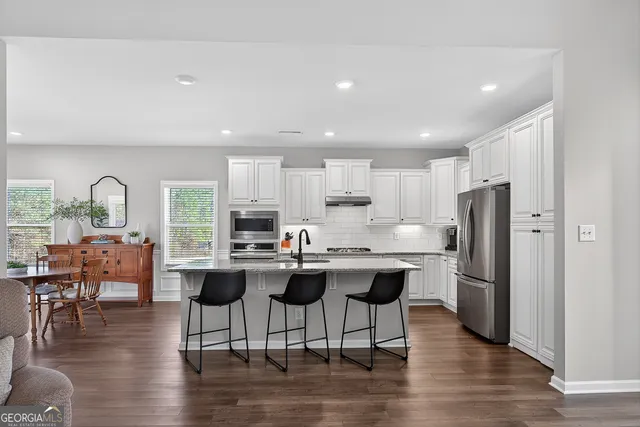 a kitchen with stainless steel appliances granite countertop a refrigerator a stove a sink a dining table and chairs with wooden floor