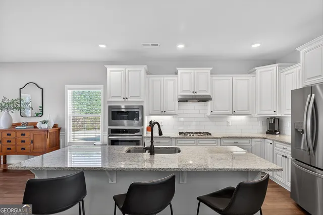 a kitchen with stainless steel appliances granite countertop a stove a sink a refrigerator and white cabinets