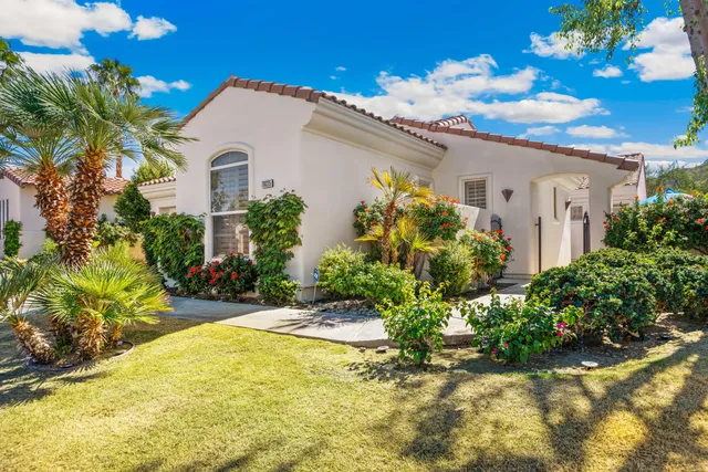 a view of a white house with a big yard and flower plants