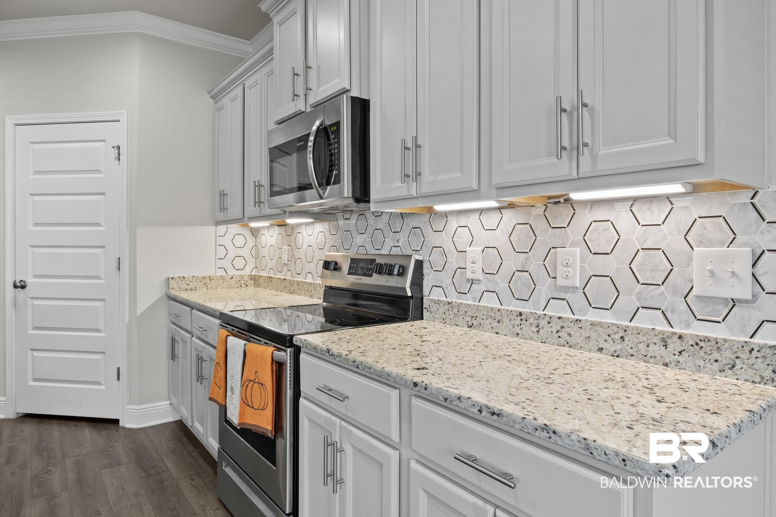 2050 Bourbon Street Foley, AL 36535 - Photo 16 of 32 Kitchen with dark wood-type flooring, white cabinets, ornamental molding, light stone counters, and stainless steel appliances