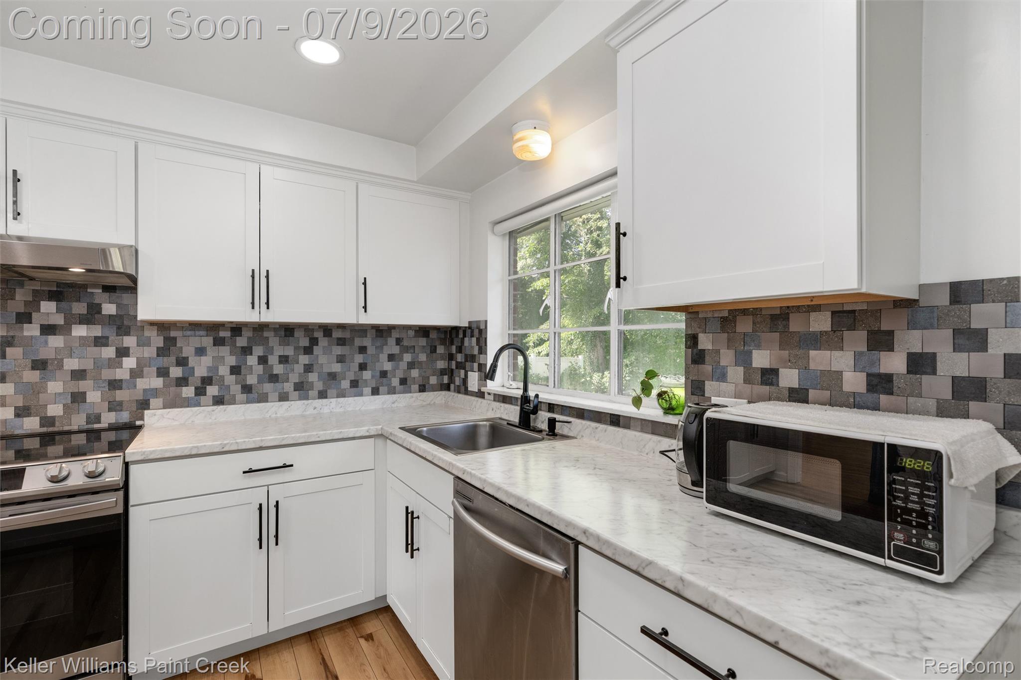 2731 Crooks Road Royal Oak, MI 48073 - Photo 16 of 34 Kitchen featuring white shaker-style cabinetry with black hardware, mosaic tile backsplash, light-colored countertops, stainless steel appliances, and wood-finish flooring
